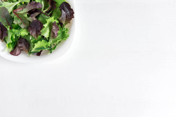 Salaatti lehdet valkoisella lautasella valkoisella taustalla. Kevyt bannerikehys. Vegaanibanderolli. Näkymä ylhäältä
 - Valokuva, kuva