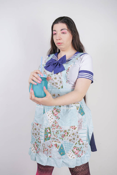 encantadora chica de anime de tamaño grande en uniforme escolar y un delantal en la parte superior con una lata azul de bebida sobre fondo blanco
 - Foto, Imagen