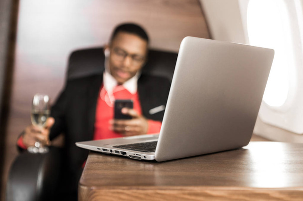 Attractive and successful African American businessman with glasses working on a laptop while sitting in the chair of his private jet - Фото, изображение