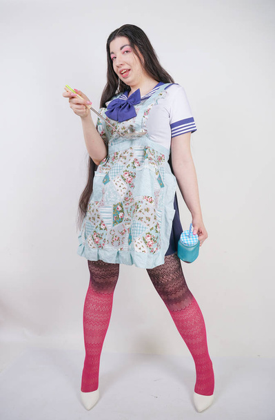encantadora chica de cocina morena en uniforme de escuela de anime y delantal de cocina sobre fondo blanco en Studio
 - Foto, Imagen