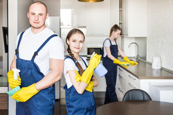 Cleaning service with professional equipment during work. professional kitchenette cleaning, sofa dry cleaning, window and floor washing. man and women in uniform, overalls and rubber gloves - 写真・画像