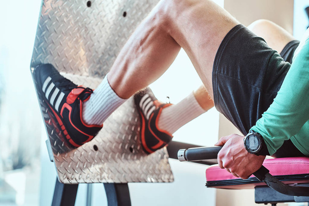 Активний чоловік робить вправи ногами на тренувальному апараті в тренажерному залі
 - Фото, зображення