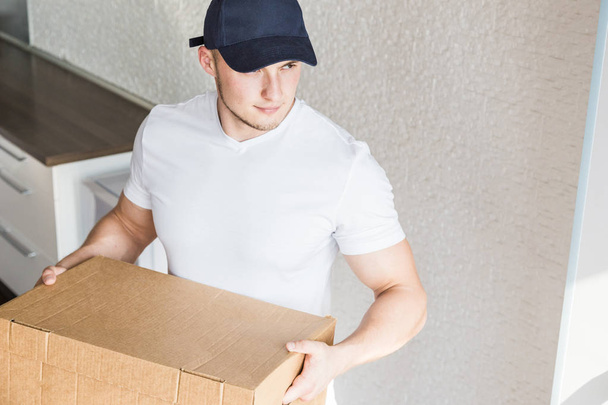 Delivery strong, muscular man loading cardboard boxes for moving to an apartment. professional worker of transportation, male loaders in overalls. free space for text, isolated - Zdjęcie, obraz