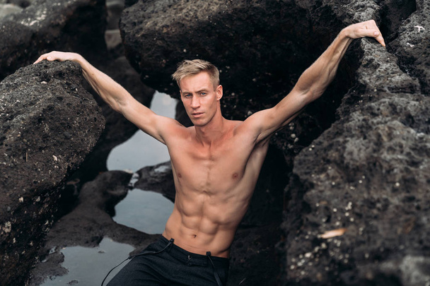 Portrait of sexy guy with bare-chested rests on beach with black sand - Foto, Bild