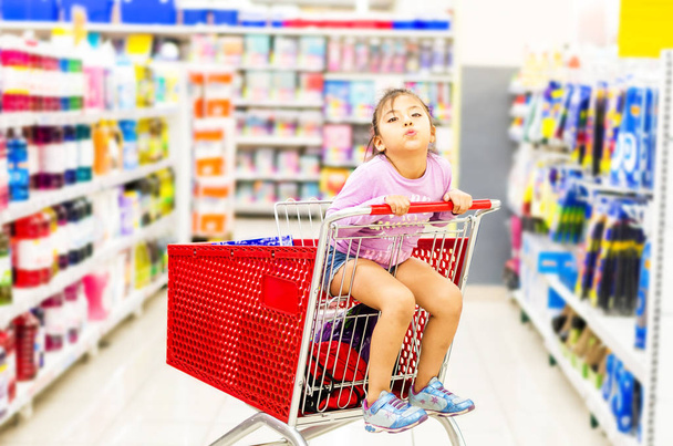 sale, consumerism and people concept - happy little girl in shopping cart - Photo, Image