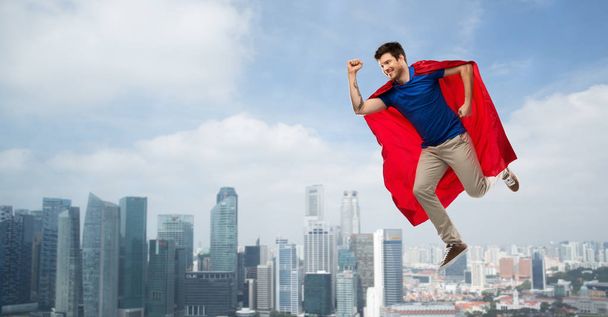 man in red superhero cape flying in air over city - Фото, изображение