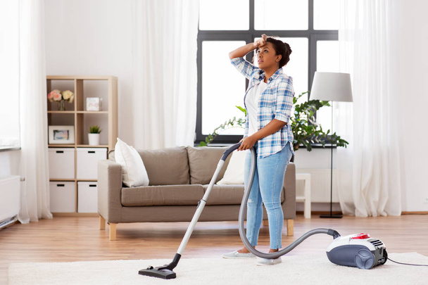 tired african woman with vacuum cleaner at home - Foto, afbeelding