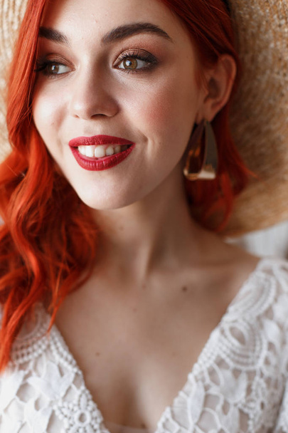 Wedding content - close-up Portrait of a young beautiful redhair girl in a hat in a studio sitting on a chair on a white background with a decorations. Copy space - Foto, afbeelding