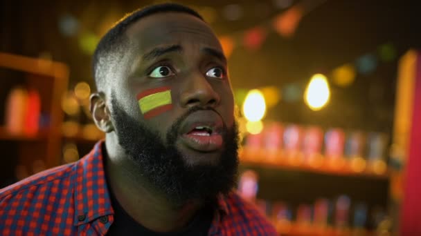 Μαύρο ισπανικό ανεμιστήρα ποδοσφαίρου με σημαία στο μάγουλο απογοητευμένος, εθνική ομάδα χάνοντας - Πλάνα, βίντεο