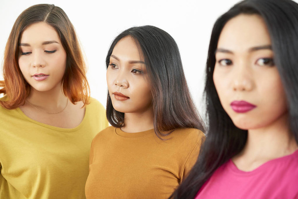 Portrait of young serious beautiful ladies looking away with Asian woman looking at camera over white background - Photo, Image