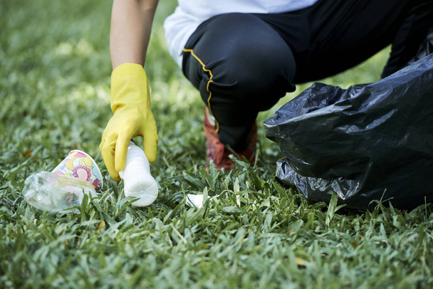 Lähikuva mies suojakäsine puhdistus vihreä ruoho roskat ja laittaa sen pussiin
 - Valokuva, kuva