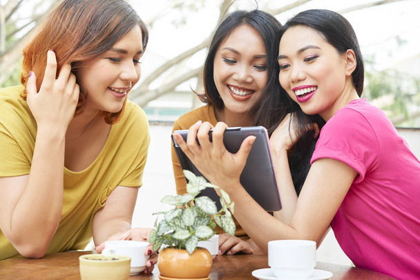 Grupo de amigas sentadas juntas no café sorrindo e se comunicando com alguém on-line usando tablet pc
 - Foto, Imagem