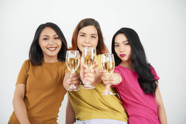 Porträt glücklicher junger Freundinnen in lässiger Kleidung, die mit Champagner auf weißem Hintergrund posieren - Foto, Bild