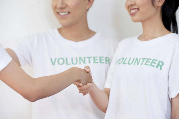 Blízcí mladí lidé s úsměvem stojí a třesou ruku a Pozdravují nového účastníka v dobrovolnické družstvu - Fotografie, Obrázek
