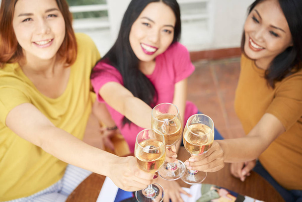 Портрет молодых друзей, пьющих бокалы шампанского и улыбающихся сидя в кафе
 - Фото, изображение