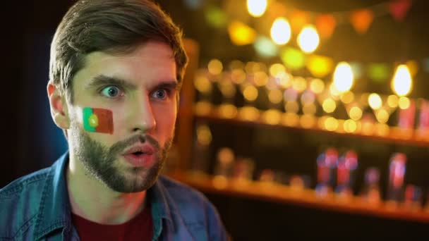 Nervöser portugiesischer Fußballfan mit Fahne auf Wange macht Facepalm, Mannschaft verliert - Filmmaterial, Video