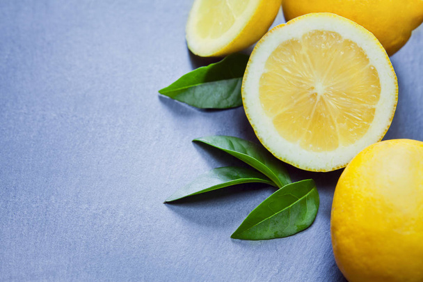 close up shot of fresh lemon slices with green leaves on gray background - Photo, image
