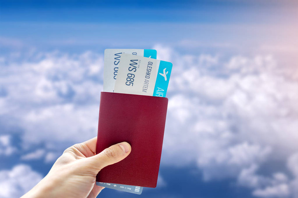 Main tenant un passeport et deux billets d'avion sur un fond bleu ciel nuageux. Voyage et vacances dans de beaux endroits
 - Photo, image