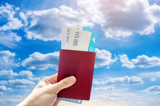 Kädessä passi ja kaksi lentolippua sinisellä taustalla pilvinen taivas. Matkailu ja loma kauniissa paikoissa
 - Valokuva, kuva