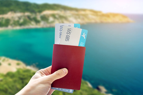 Mano con pasaporte y dos pasajes aéreos sobre un fondo azul del mar. Viajes y vacaciones en lugares exóticos
 - Foto, imagen