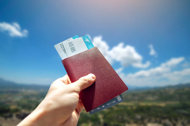 Рука тримає паспорт і два авіаквитки на синьому тлі хмарного неба. Подорожі та відпустка в красивих місцях
 - Фото, зображення