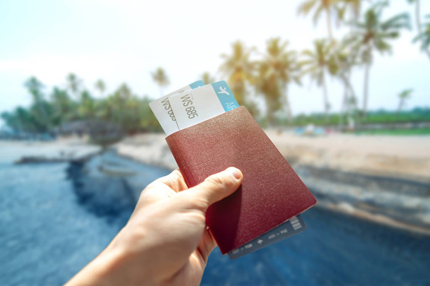 Hand holding a passport and two air tickets on a blue background of the sea. Travel and vacation in exotic places - Фото, изображение