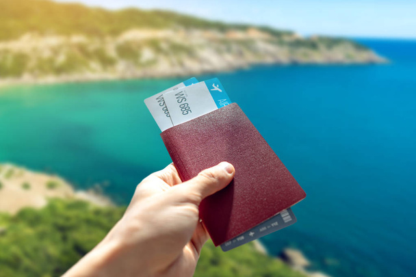 Hand holding a passport and two air tickets on a blue background of the sea. Travel and vacation in exotic places - Photo, Image