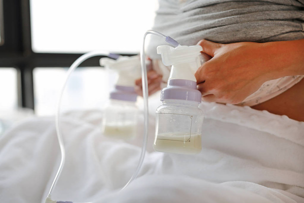 Close-up mother using automatic breast pump on the bed. - Foto, Bild
