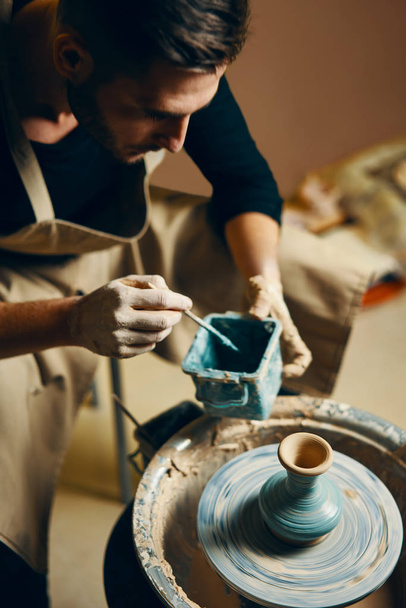 Man painting handmade pottery at ceramic workshop. Art concept - 写真・画像