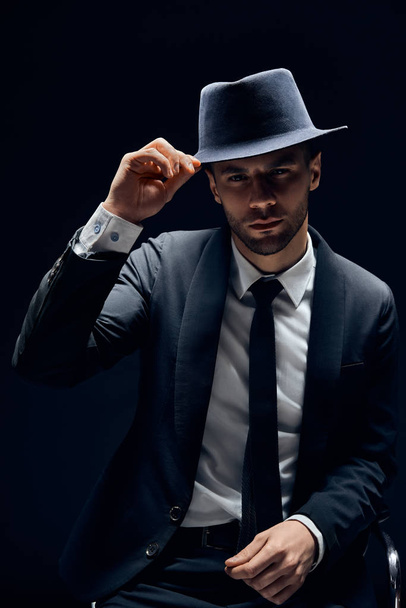 Young handsome man in black suit touch his hat on dark background. Man beauty, greeting concept                                  - Photo, Image