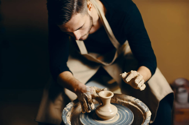 Man potter working on potters wheel making ceramic pot from clay in pottery workshop. art concept - Fotó, kép