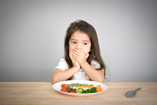 Nutrition & healthy eating habits for kids concept. Children do not like to eat vegetables. Little cute kid half race girl refuse to eat healthy vegetables. - Foto, immagini