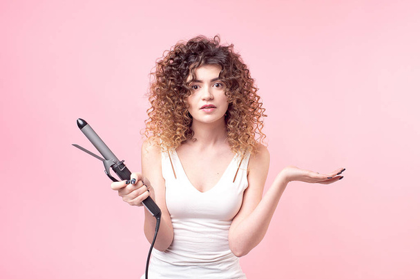 Beautiful woman with amazing curls in white shirt holds styling accessories in hand. Hair styling set with curling accessories - Foto, Imagem