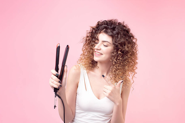 Beautiful woman with a smile on face with amazing curls in a white t-shirt holds in her hand accessories for styling and curling hair - Photo, image