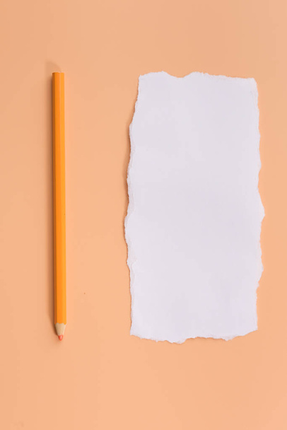 A piece of white torned paper over orange background with pencil - Photo, Image