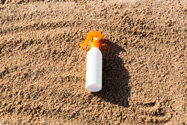Suntan lotion white bottle on sand with copy space. sunblock spf cream on the sea beach in summer vacation concept - Photo, Image