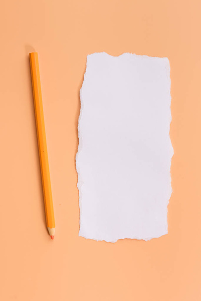 A piece of white torned paper over orange background with pencil - Foto, Bild
