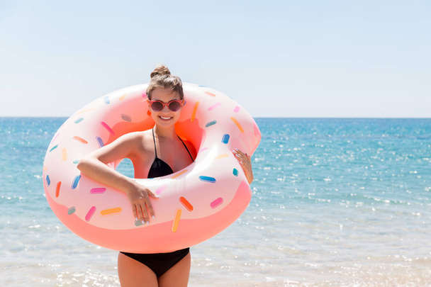 女性は夏の晴れた日にビーチでインフレータブルドーナツで泳いでいます。夏休みと休暇のコンセプト - 写真・画像