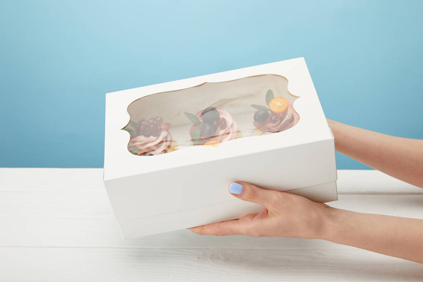 vue partielle de femme tenant boîte avec cupcakes isolé sur bleu
 - Photo, image