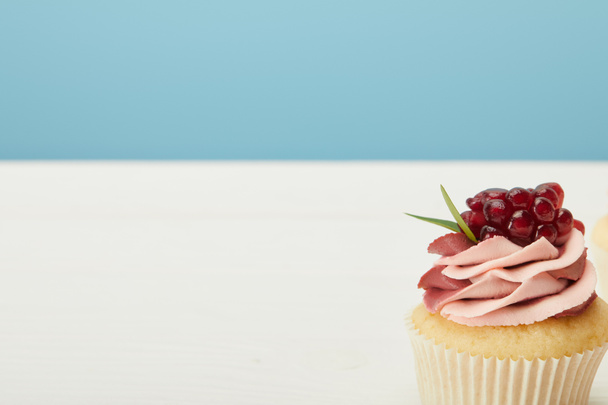 tasty cupcake with garnet and cream on white surface isolated on blue - Photo, image