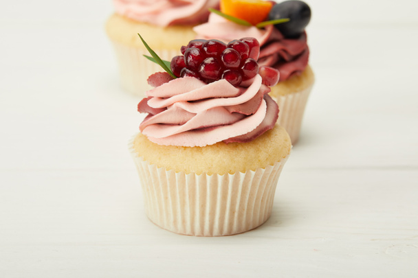 selective focus of cupcakes with cream and berries on white surface - Zdjęcie, obraz