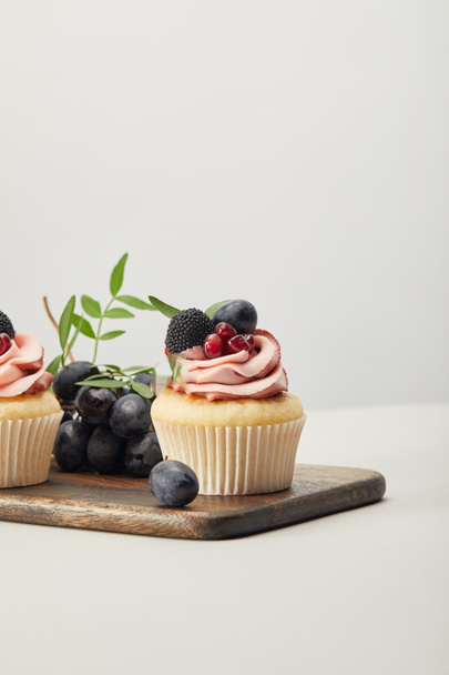 wooden cutting board with sweet cupcakes isolated on grey - 写真・画像