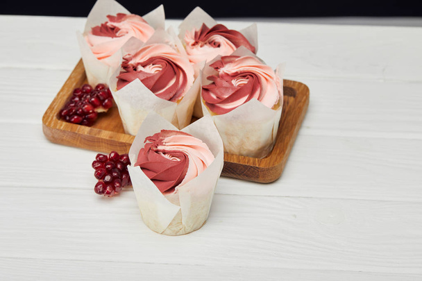 beyaz yüzeyüzerinde kesme tahtası üzerinde krem ve garnet ile cupcakes - Fotoğraf, Görsel