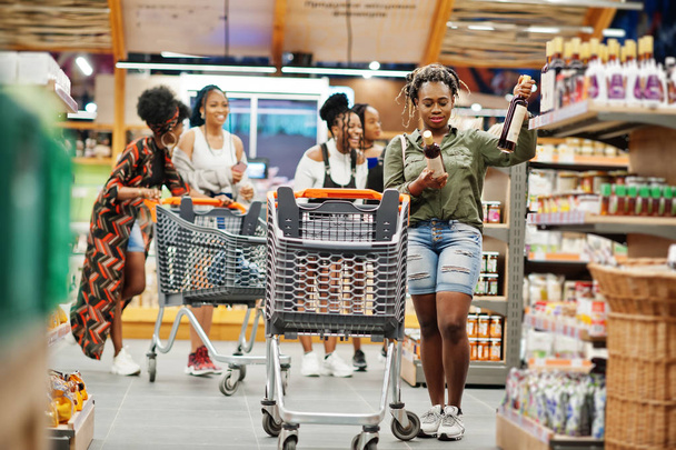 African woman choose wine at supermarket against her afro friend - Foto, Imagen