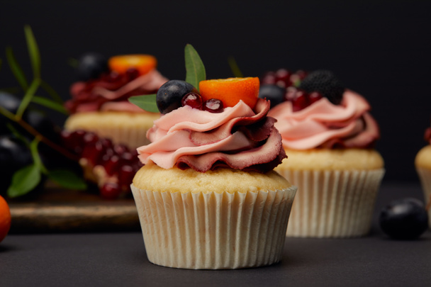 cupcakes with fruits and berries on grey surface isolated on black - Foto, immagini
