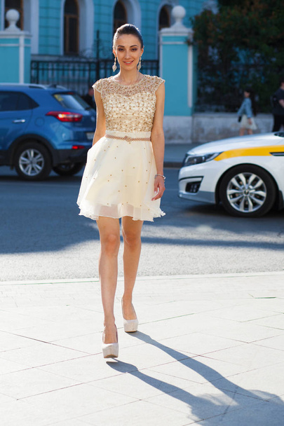Young beautiful brunette woman in white dress walking on the str - 写真・画像