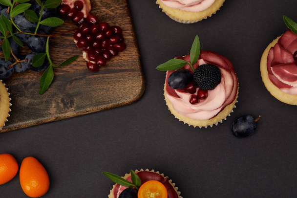 vista superior de cupcakes, uvas, granate y tabla de cortar en la superficie negra
 - Foto, imagen