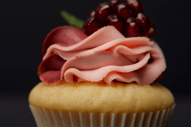 close up view of cupcake with cream and garnet on black - Фото, зображення