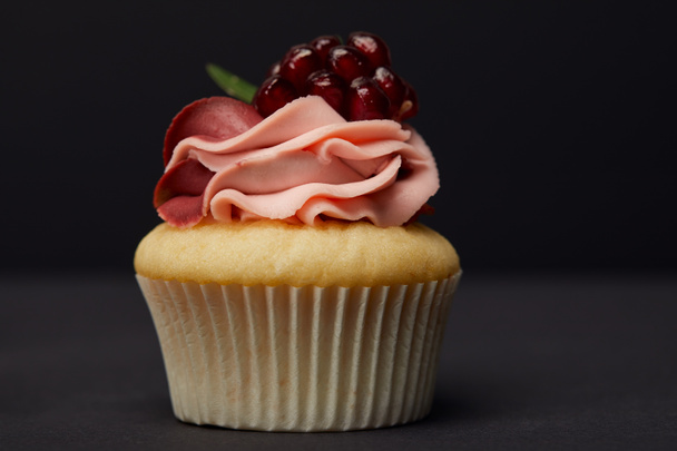 sweet cupcake with cream and garnet on grey surface isolated on black - Photo, Image