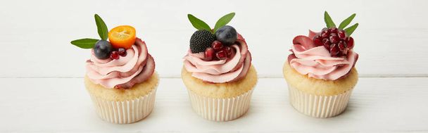 panoramic shot of cupcakes with fruits and berries on white surface - Foto, Imagem